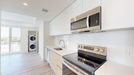 Located in Los Angeles at 139 Occidental Blvd, this modern 1-bedroom, 1-bathroom unit offers a thoughtfully designed layout across a single floor. The open-concept kitchen and living area serves as the heart of the unit, featuring light wood-tone cabinetry, stainless steel appliances including a refrigerator, range, microwave, and dishwasher, and clean white countertops. Light hardwood flooring runs throughout the main living areas, lending a warm, contemporary feel. A dedicated in-unit laundry closet with a stacked washer and dryer adds everyday convenience. The bedroom is a comfortable, well-proportioned retreat finished with soft carpet flooring and a large sliding-door closet offering ample storage. A window frames views of the surrounding Los Angeles skyline and palm trees, filling the room with natural light. The living area provides direct access to a private balcony through sliding glass doors, offering open views of the neighborhood's iconic palm tree-lined scenery. The bathroom features a full tub and shower combo enclosed by sleek sliding glass doors, a wood-toned vanity with a white countertop, and light tile flooring. Clean white walls, recessed lighting, and a minimalist aesthetic define the overall ambiance of the space.