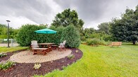Located at 600 North Lilac Drive in Golden Valley, Minnesota, this expansive outdoor community space offers a well-rounded array of amenities across a generously sized single-level grounds. The centerpiece is a charming circular paver patio framed by manicured hedges, mature trees, and colorful mulched garden beds, furnished with wooden Adirondack chairs and a shaded picnic table — an inviting spot for relaxed outdoor gatherings. Adjacent to the patio, raised wooden garden beds are actively cultivated with a variety of herbs and plants, offering a productive green space for residents. A dedicated dog agility area features a gravel surface enclosed by chain-link fencing, complete with agility equipment including a jump hoop, providing a safe and engaging space for pets. Additional gravel areas with seating benches offer flexible open-air recreation space. The lush lawn stretches throughout, lined with dense natural plantings, wildflower borders, and mature trees that provide shade and privacy. The brick building exterior is adorned with climbing ivy, adding a classic, established character to the setting. A paved walkway and parking area provide convenient access, rounding out this thoughtfully designed and well-maintained outdoor community environment.