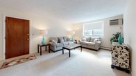Located at 17 Conant in Beverly, MA, this single-floor residence offers a well-organized layout designed for comfortable everyday living. The kitchen is equipped with dark wood cabinetry, a coil electric range with overhead ventilation, a stainless steel sink, and white tile backsplash, providing a practical and efficient cooking space. The living room is bright and welcoming, featuring neutral carpet, soft wall tones, and a window that brings in natural light, creating an open and relaxed atmosphere. Adjacent to the living area, the formal dining room is anchored by an elegant chandelier overhead and offers generous space for entertaining. The primary bedroom is a calm retreat with plush carpeting, a large window with outdoor views, and ample room for furnishings. A second bedroom provides flexibility as a guest room or home office, also carpeted and naturally lit. The bathroom is well-appointed with a full tub and shower combination, mosaic tile flooring, grab bar accessibility features, and a single vanity. Additional closet storage is accessible throughout the unit. The overall interior palette of soft neutrals and warm wood tones creates a cohesive, understated ambiance throughout the home.