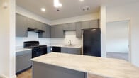 This single-floor residence offers a thoughtfully designed layout with modern finishes throughout. The kitchen serves as the heart of the space, showcasing gray shaker-style cabinetry, light marble-look countertops, and a full suite of black appliances including a gas range, dishwasher, and refrigerator. A generously sized kitchen island with pendant lighting above provides additional prep space and casual seating, while light wood-look flooring ties the area together seamlessly.

The bedrooms feature plush carpeting and large windows fitted with horizontal blinds, allowing an abundance of natural light and offering pleasant views of surrounding greenery. The neutral wall tones and clean lines create a calm, functional atmosphere in each room.

The bathrooms continue the gray cabinetry theme, each equipped with marble-look countertops and a single vanity with a mirror. One bathroom features a tub-shower combination with warm earth-toned tile surround and wood-look flooring, while another includes a built-in closet with multi-tier shelving for convenient storage. The consistent use of soft neutrals and coordinated fixtures throughout the space creates a cohesive, modern aesthetic that is both practical and visually appealing.