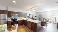 Located in the heart of Wilmington, Delaware, this single-floor residence offers a thoughtfully designed open-concept layout that seamlessly connects the kitchen, dining, and living areas. The kitchen is a standout feature, equipped with rich dark-toned cabinetry, stainless steel appliances including a refrigerator, microwave, and range, complemented by a patterned tile backsplash and light quartz countertops. A peninsula island provides additional prep space and doubles as a casual dining area, while warm hardwood-style flooring runs throughout the main living spaces, adding continuity and warmth. The living area is bright and welcoming, with clean white walls that serve as a neutral backdrop for décor, and windows that invite natural light. Two bedrooms offer comfortable retreats; one features carpet flooring and a large window with urban views, while the other showcases hardwood-style floors and ample natural light. The bathroom is well-appointed with dark wood cabinetry, a white countertop vanity, wood-look flooring, and a tiled shower-tub combination. The overall aesthetic is modern and cohesive, with consistent use of dark wood tones, neutral palettes, and contemporary fixtures throughout the entire space.
