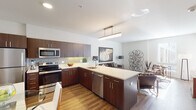 Located in the heart of Wilmington, Delaware, this single-floor residence offers a thoughtfully designed open-concept layout that seamlessly connects the kitchen, dining, and living areas. The kitchen is a standout feature, equipped with rich dark-toned cabinetry, stainless steel appliances including a refrigerator, microwave, and range, complemented by a patterned tile backsplash and light quartz countertops. A peninsula island provides additional prep space and doubles as a casual dining area, while warm hardwood-style flooring runs throughout the main living spaces, adding continuity and warmth. The living area is bright and welcoming, with clean white walls that serve as a neutral backdrop for décor, and windows that invite natural light. Two bedrooms offer comfortable retreats; one features carpet flooring and a large window with urban views, while the other showcases hardwood-style floors and ample natural light. The bathroom is well-appointed with dark wood cabinetry, a white countertop vanity, wood-look flooring, and a tiled shower-tub combination. The overall aesthetic is modern and cohesive, with consistent use of dark wood tones, neutral palettes, and contemporary fixtures throughout the entire space.