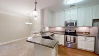 Located at Greystone Summit Drive in Cumming, Georgia, this well-appointed 2-bedroom, 2-bathroom single-story home offers a thoughtfully designed layout with a warm, neutral palette throughout. The open-concept kitchen is a standout feature, showcasing granite countertops, white beadboard cabinetry, stainless steel appliances, hardwood flooring, and a peninsula with bar seating — all illuminated by stylish pendant lights and an adjacent chandelier that bridges the kitchen to the dining area. The combined dining and living room is generously sized, highlighted by a tray ceiling with crown molding and a ceiling fan, creating an elevated sense of space and comfort. The dining area features wainscoting and its own chandelier, adding a refined touch. The spacious primary bedroom connects directly to a private en-suite bathroom and offers a ceiling fan and natural light. Both bedrooms are carpeted and well-proportioned, with the primary suite providing direct access to additional rooms. The bathrooms are clean and functional, with one featuring a soaking tub and large wall mirror. The home also includes a dedicated laundry room with washer/dryer hookups, a pantry, a utility room, and five closets, providing exceptional storage. Crown molding and consistent finishes lend a polished look throughout.