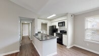 This single-story residence offers a well-organized layout with a variety of thoughtfully designed spaces throughout. The open-concept kitchen serves as a functional centerpiece, featuring white cabinetry, dark countertops, a kitchen island with an integrated sink, and black appliances including a refrigerator, range, and microwave. A dedicated laundry area with a washer is conveniently accessible directly from the kitchen. Hardwood-style flooring runs throughout the main living and kitchen areas, contributing to a clean, cohesive aesthetic.

The living room is a standout space, characterized by soaring vaulted ceilings, a ceiling fan, and a curved bay window arrangement that invites abundant natural light. The open feel is further enhanced by the room's generous proportions and neutral wall tones.

Bedrooms are carpeted for comfort, with at least one featuring vaulted ceilings and a prominent arched window that frames outdoor views. Additional bedrooms are well-proportioned with standard ceilings and natural light from individual windows.

Two bathrooms are present: one with a single-sink vanity, dark countertop, white cabinetry, and a glass-enclosed shower, and a second full bathroom with a tub-shower combination and matching vanity. Both bathrooms feature hardwood-style flooring and neutral finishes throughout.