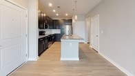 Located at 115 Great Lawn Dr in Summerville, South Carolina, this single-story home offers a well-designed, open-concept layout that maximizes functionality and style. The kitchen serves as a standout centerpiece, featuring rich dark shaker-style cabinetry paired with striking granite countertops, a large central island with pendant lighting and a built-in sink, white subway tile backsplash, and a full suite of stainless steel appliances including a refrigerator, range, and microwave. Light wood-look flooring runs throughout the main living areas, creating a clean and cohesive aesthetic. The bathroom continues the dark cabinetry theme with a granite-topped vanity, a tall linen tower cabinet, and light wood-look tile flooring, offering both storage and a polished finish. The bedroom is carpeted for comfort and is well-lit by dual windows with blinds that invite natural light while providing privacy. Neutral gray walls throughout the home create a versatile backdrop suitable for a variety of interior styles. The floorplan, visible in the overhead dollhouse view, reveals a thoughtfully arranged layout with arched interior doorways adding an architectural charm. This home combines modern finishes with practical design for comfortable, everyday living.