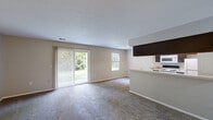 This single-floor, one-bedroom, one-bathroom unit offers a practical and well-organized layout across a comfortable footprint. The open-concept living and kitchen area forms the heart of the space, with plush carpeting throughout the living area and a neutral color palette that creates a bright, cohesive atmosphere. A sliding glass door fitted with vertical blinds fills the living room with natural light and provides direct views of lush greenery, complemented by an additional window that further brightens the space.

The galley-style kitchen features dark espresso cabinetry on both sides, light countertops, and wood-look flooring, offering efficient functionality. A raised breakfast bar peninsula separates the kitchen from the living area, while a recessed tray ceiling detail adds a subtle architectural element overhead. White appliances, including a range, refrigerator, built-in microwave, and dishwasher, provide full functionality.

The carpeted bedroom offers a comfortable amount of space and includes a mirrored sliding closet door, adding a sense of depth to the room. The bathroom is finished with dark cabinetry beneath a single-sink vanity, a full tub-shower combination, and wood-look tile flooring, providing a clean, functional design.