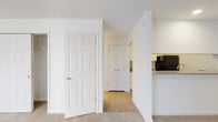 Located at 1113 Powers Ferry Pl in Marietta, GA 30067, this single-floor unit offers a clean, functional layout designed for comfortable everyday living. The interior features a neutral color palette throughout, with white walls and textured ceilings that keep the space feeling fresh and bright.

The living area is carpeted and generously sized, with an open flow that connects seamlessly to the kitchen. A half-wall peninsula separates the two spaces, providing both visual openness and a practical countertop surface. The kitchen is equipped with white cabinetry, light countertops, a black refrigerator, and additional black appliances, with light wood-look flooring that adds a warm contrast to the cabinetry.

The bedroom area benefits from natural light through a large window fitted with horizontal blinds, offering views of surrounding greenery. A wall-unit HVAC system ensures climate control. Two closets with built-in hanging rods provide substantial storage within the bedroom space.

The hallway connects the main living areas to the bathroom, which features a full tub-shower combo with white tile surround, chrome fixtures, and wood-look flooring. Six-panel white doors are used consistently throughout, contributing to a cohesive interior aesthetic. The overall layout is practical and well-organized, making efficient use of the available space.