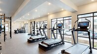This modern fitness center is thoughtfully designed to support a full spectrum of workout routines, offering distinct zones for cardio, strength training, and functional fitness. The cardio area features a row of treadmills and ellipticals by Freemotion, each equipped with interactive touchscreen displays, positioned along expansive floor-to-ceiling windows that flood the space with natural light and offer views of the surrounding exterior. The open layout is reinforced by recessed ceiling lighting and durable rubber flooring throughout.

The strength and functional training zone is anchored by a substantial multi-station Freemotion power rack system, complete with cable attachments, battle ropes, medicine balls, plyo boxes, and kettlebells in varying weights. Full-length wall mirrors line multiple sections of the space, enhancing the sense of openness and allowing users to monitor their form during exercise. A comprehensive free weights area includes a wide selection of dumbbells organized on tiered racks alongside adjustable benches.

Selectorized strength machines round out the equipment offerings, providing options for targeted muscle training. The overall ambiance is clean, professional, and energizing, combining a contemporary aesthetic with a practical, high-performance environment suited for a wide range of fitness goals.