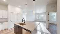 This well-designed single-story residence offers two bedrooms, two bathrooms, and two closets within a thoughtfully arranged floor plan. The open-concept living and kitchen area serves as the heart of the home, where light hardwood flooring, neutral white walls, and elevated ceilings create a bright, airy atmosphere. Natural light flows freely into the living area through windows overlooking the outdoors.

The kitchen is a standout feature, centered around a generous island with a quartz countertop, an undermount sink, and a matte black pull-down faucet. Two pendant lights hang above the island, adding a modern touch. White shaker cabinetry with black hardware, a herringbone tile backsplash, and stainless steel appliances complete the space.

Both bedrooms feature the same light hardwood flooring and clean white walls. The primary bedroom includes a dedicated walk-in closet with wire shelving systems for organized storage. The primary bathroom offers a double-sink vanity with quartz countertops, a large framed mirror, matte black fixtures, and direct access to the walk-in closet. A second closet with wire shelving provides additional storage. The overall aesthetic throughout is clean, contemporary, and move-in ready.