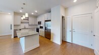 Located at 305 Oberlin Rd in Raleigh, NC, this single-floor residence offers a well-designed, open-concept layout with modern finishes throughout. The kitchen is a standout feature, showcasing white shaker cabinetry, a herringbone-patterned tile backsplash, granite countertops, a large central island with pendant lighting, and a full suite of stainless steel appliances including a range, microwave, dishwasher, and French door refrigerator. Warm hardwood-style flooring flows seamlessly through the kitchen and living areas, where a ceiling fan and sliding glass doors open to a private balcony with views of the surrounding neighborhood. The bedrooms are carpeted for comfort and equipped with ceiling fans and generous natural light from large windows. Each bedroom provides access to a walk-in closet featuring multi-tier shelving and hanging rods for ample storage. The bathrooms are well-appointed, with one offering a soaking tub surrounded by clean white subway tile and brushed nickel fixtures, and another featuring a glass-enclosed stand-up shower, granite vanity, and hardwood-style flooring. The overall aesthetic is clean, contemporary, and move-in ready.