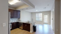 This single-floor, one-bedroom, one-bathroom unit offers a thoughtfully designed open-concept layout that maximizes its functional living space. The kitchen serves as a central highlight, featuring rich dark-wood cabinetry extending to the ceiling, granite countertops, a mosaic tile backsplash in muted blue and grey tones, and a full suite of stainless steel appliances including a range, refrigerator, microwave, and dishwasher. A peninsula with a single-basin sink provides additional prep space and naturally delineates the kitchen from the adjoining living area.

The living area is finished with light hardwood-style flooring that enhances the brightness of the space, complemented by large windows and a private exterior door that invites natural light and outdoor access. Neutral grey walls maintain a clean, cohesive aesthetic throughout.

The bedroom is carpeted for comfort, features a dedicated closet, and is naturally lit by a window with exterior views. The bathroom is equipped with a full soaking tub and shower combination, accessibility grab bars, wood bath bench, granite-topped vanity, and hardwood-style flooring, reflecting both practicality and thoughtful design.