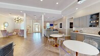 The Azalea Ridge Apartments leasing office at 1400 Boxwood Blvd in Columbus, Georgia, is a thoughtfully designed single-floor space that blends elegance with functionality. Upon entry, guests are greeted by a grand foyer with arched windows and French doors that invite natural light throughout. The herringbone-patterned hardwood flooring flows seamlessly across the entire space, adding a refined architectural detail underfoot.

The reception area serves as the heart of the office, featuring a wide, sleek front desk adorned with textured paneling and branded Azalea Ridge signage. Decorative gold fish-scale wall art and subtle wallcoverings add warmth and character to the workspace. A flat-screen monitor and informational displays ensure visitors have access to key community details.

Adjacent to the reception desk is a well-appointed kitchenette station with gray cabinetry, herringbone tile backsplash, and open shelving — ideal for welcoming residents and prospects alike.

The lounge area offers a sophisticated sitting space with a tufted velvet sofa, curated accent chairs, a glass and gold coffee table, and an animal-print area rug. Bold artwork and sculptural décor pieces enhance the upscale ambiance. Tray ceilings with recessed lighting add depth and refinement throughout, while large windows and glass-paned French doors provide lush outdoor views, completing the polished, inviting atmosphere.