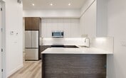 Located at 10125 114 Street NW, this well-appointed 2-bedroom, 2-bathroom unit offers a thoughtfully designed single-floor layout with modern finishes throughout. Light wood-tone laminate flooring runs continuously across the living spaces, creating a clean and cohesive aesthetic.

The kitchen is a standout feature, boasting two-tone cabinetry with white upper cabinets reaching to the ceiling and dark wood-grain lower cabinets paired with stainless steel appliances, including a refrigerator, electric range, and over-the-range microwave. A peninsula with a white quartz countertop provides additional workspace and a natural transition into the living area.

Both bathrooms are finished with large-format marble-look tile flooring and walls, paired with dark wood-grain vanities and white quartz countertops. One bathroom features a glass-enclosed shower, while the second includes a full soaker tub, offering functional variety.

The bedrooms are bright and minimalist, featuring light-filtering roller blinds and light wood flooring. The primary bedroom includes a sliding door for added privacy and natural light, while the second bedroom offers a dedicated window with views to the surroundings. Clean white walls throughout the unit enhance the sense of openness and light in this efficiently planned modern home.