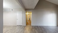This single-floor unit at 1803 Campbell Pkwy in Joplin, Missouri offers a well-organized layout connecting several distinct living areas through a central hallway finished with wood-look flooring and neutral walls. The living room is a standout feature, showcasing dramatic vaulted ceilings and a floor-to-ceiling tile-surround fireplace that anchors the space with character. Sliding glass doors open to a private balcony, bringing in natural light and outdoor views. The adjoining dining area is illuminated by a chandelier, adding a touch of elegance to the open transition between living and eating spaces. The galley-style kitchen is efficiently designed with warm honey-toned cabinetry, granite-look countertops, a double sink, and black appliances including a refrigerator, electric range, and dishwasher. Bedrooms are comfortably sized, each featuring wood-look flooring, neutral paint, and either ceiling fans or windows with blinds for natural light. One bedroom includes its own sliding door to a balcony. The bathrooms are functional and clean, each equipped with a tub-shower combination and wood-look flooring. Textured ceilings are consistent throughout, adding a classic residential feel to the overall space.