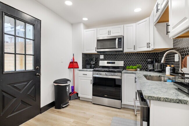 Cocina con cubo de basura, artículos de limpieza y puerta al patio trasero. - 10 Carrie St