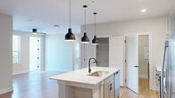 Located at 135 Ballentrae Ct in Chapel Hill, NC, this well-appointed single-story home offers 3 bedrooms and 2 bathrooms across a thoughtfully designed floor plan. The open-concept kitchen serves as the heart of the home, showcasing a large center island with a white quartz countertop, an undermount sink with a matte black faucet, and three striking black pendant lights overhead. Light gray shaker-style cabinetry, a subway tile backsplash, and stainless steel appliances — including a refrigerator, range, and over-the-range microwave — complete the kitchen. A dedicated pantry closet provides additional storage. The kitchen flows seamlessly into the living area, where warm-toned hardwood flooring adds continuity. The bedrooms offer a mix of hardwood and plush carpet flooring, ceiling fans, and windows that bring in natural light and outdoor views. The primary bedroom is generously proportioned with its own dedicated space. The bathrooms are finished in a clean, modern style, with the main bathroom featuring a dual-sink vanity with white cabinetry, a wide framed mirror, matte black fixtures, and hardwood flooring. A dedicated laundry room with side-by-side washer and dryer and built-in shelving adds everyday convenience. Throughout, neutral tones and modern hardware create a cohesive, contemporary ambiance.