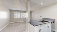 Located at 837-845 16th St in San Diego, CA, this one-bedroom, one-bathroom residence offers a practical and well-organized single-floor layout. The open-concept kitchen and living area form the heart of the home, where a peninsula counter with a dark granite-style surface and undermount sink separates the kitchen from the carpeted living space. The kitchen is equipped with stainless steel appliances — including a refrigerator, electric range, and over-the-range microwave — complemented by white cabinetry and wood-look vinyl flooring. Natural light filters into the living area through slatted blinds on a double window, lending the space a bright, airy feel against the neutral warm-beige walls and textured ceiling. The bedroom is a well-proportioned, carpeted retreat featuring a window with exterior views and a mirrored sliding-door closet with built-in shelving for organized storage. The bathroom is clean and functional, featuring a full tub-shower combination with tile surround, a white vanity with a dark countertop and undermount sink, and wood-look vinyl flooring. Throughout the residence, a consistent neutral color palette and modern fixtures create a cohesive, move-in-ready environment suited for comfortable urban living in downtown San Diego.