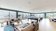 Located at 141 Danbury Road in Wilton, CT, this thoughtfully designed amenity lounge is a single-floor space that delivers an upscale, resort-inspired atmosphere. The open layout is anchored by a bold coastal color palette — deep teal accent walls and vibrant blue patterned rugs contrast beautifully with warm natural wood elements and light herringbone hardwood flooring throughout.

The space is divided into distinct functional zones. A lounge area near the entrance features a linear gas fireplace framed by geometric tile, built-in wood shelving, and comfortable seating arranged around a round white coffee table. Adjacent to this is a billiards area centered on a full-size pool table, complemented by a round dining table with woven rattan chairs and a wall-mounted cue rack.

A wet bar area showcases a striking slatted wood accent wall, bold blue hexagonal tile, a white stone countertop, and three oversized brass pendant lights. An additional seating zone along the glass-wrapped perimeter offers multiple lounge chairs and curved sofas, bathed in natural light from expansive floor-to-ceiling windows that frame views of the surrounding buildings and greenery. Recessed lighting and curated artwork complete this well-appointed communal retreat.