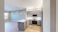 Located at 1820 Hickory St in Dallas, TX, this modern one-bedroom, one-bathroom residence offers a thoughtfully designed single-floor layout with contemporary finishes throughout. The open-concept living and kitchen area serves as the heart of the home, featuring light oak hardwood flooring, recessed lighting, and a wall-mounted linear fireplace that adds warmth and style to the living space. The kitchen is well-appointed with sleek gray cabinetry, white quartz countertops, a peninsula with an undermount sink, and a full suite of stainless steel appliances including a range, microwave, dishwasher, and refrigerator. Stylish pendant lights hang above the peninsula, enhancing the modern aesthetic. Cool blue-gray walls create a calm, cohesive palette throughout the unit. The bedroom is a comfortable retreat with recessed lighting, a ceiling fan, and large windows that frame impressive views of the Dallas downtown skyline. A private door from the bedroom provides additional access. The bathroom features light tile flooring and a clean, functional layout. A hallway connects the spaces efficiently, and a closet provides convenient storage. The overall ambiance is bright, contemporary, and move-in ready, making this a polished urban residence in the heart of Dallas.