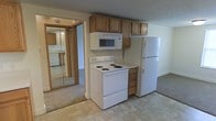 This two-floor residential space offers a practical and functional layout designed for comfortable everyday living. The kitchen serves as a central feature, equipped with white appliances including a coil-burner electric range, an over-the-range microwave, and a full-size refrigerator. Warm-toned wood cabinetry provides overhead storage, framing the appliances neatly and adding a traditional character to the space. The kitchen floor features a light-toned tile, creating a clean, easy-to-maintain surface underfoot.

Adjacent to the kitchen, a mirrored closet door is visible, reflecting the surrounding space and contributing a sense of depth and openness to the area. The flooring transitions to carpet in the neighboring room, adding warmth and comfort to the living areas. Neutral-toned walls throughout give the space a clean, understated appearance that can easily accommodate a variety of furnishing styles.

The two-floor layout provides separation between living and private areas, offering functional zoning throughout the home. Overall, the space presents a straightforward, well-organized environment with the essential features needed for day-to-day residential use.
