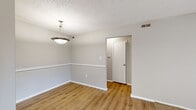 Located at 3500 Pelham Rd in Greenville, SC, this one-bedroom, one-bathroom unit offers a well-organized single-floor layout with a functional blend of hard surface and carpeted flooring throughout. The combined living and dining area is welcoming, featuring warm wood-look laminate flooring, a classic chair rail detail along the walls, and a pendant light fixture that defines the dining space. A sliding glass door in the living area fills the room with natural light and provides views of the outdoors. The kitchen is a standout feature, equipped with dark cabinetry, a mosaic tile backsplash, a double sink, and black appliances including a range with overhead hood, offering both style and practicality. The bedroom is a comfortable, carpeted retreat with a window that allows natural light to filter in, while the walk-in closet provides ample storage with a full-width shelf and hanging rod. A hallway connects the rooms efficiently. The bathroom features a white vanity with a granite-style countertop, a large mirror, and an elegant three-bulb light fixture, lending a clean, polished feel. Textured ceilings and neutral-toned walls are consistent throughout, creating a cohesive and understated aesthetic.