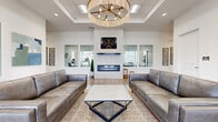 This single-story amenity center is thoughtfully designed to offer a range of community-focused spaces within a clean, contemporary aesthetic. The main lounge serves as the centerpiece, featuring a tray ceiling with a statement chandelier, a sleek linear fireplace set against a white marble surround, and gray leather sofas arranged over a woven area rug atop warm hardwood-style flooring. Large interior windows connect the lounge to adjoining spaces, promoting an open, transparent feel throughout.

The fitness center is well-appointed with multiple treadmills, a full rack system with free weights and benches, and additional cardio equipment. Abundant natural light streams through large windows fitted with blinds, while ceiling fans maintain airflow. A wall-mounted display screen and rubberized flooring complete the functional setup.

A dedicated media room offers a large wall-mounted display screen accompanied by framed movie posters, reclining leather theater-style seating, and carpeted flooring, creating a true cinematic atmosphere. Additional flexible open rooms with hardwood-style flooring and glass-paneled interior windows provide versatile space for meetings or events. The overall design is bright, modern, and cohesive throughout.