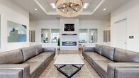 This single-story amenity center is thoughtfully designed to offer a range of community-focused spaces within a clean, contemporary aesthetic. The main lounge serves as the centerpiece, featuring a tray ceiling with a statement chandelier, a sleek linear fireplace set against a white marble surround, and gray leather sofas arranged over a woven area rug atop warm hardwood-style flooring. Large interior windows connect the lounge to adjoining spaces, promoting an open, transparent feel throughout.

The fitness center is well-appointed with multiple treadmills, a full rack system with free weights and benches, and additional cardio equipment. Abundant natural light streams through large windows fitted with blinds, while ceiling fans maintain airflow. A wall-mounted display screen and rubberized flooring complete the functional setup.

A dedicated media room offers a large wall-mounted display screen accompanied by framed movie posters, reclining leather theater-style seating, and carpeted flooring, creating a true cinematic atmosphere. Additional flexible open rooms with hardwood-style flooring and glass-paneled interior windows provide versatile space for meetings or events. The overall design is bright, modern, and cohesive throughout.