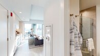 Located at 354 N Union Ave in Chicago's vibrant West Loop neighborhood, this single-floor residence showcases a refined contemporary design with an open-concept layout and high-end finishes throughout. Light hardwood-style flooring flows seamlessly across the space, complementing the bright, neutral palette that defines each area.

The living room serves as the heart of the home, anchored by a textured white tile accent wall that frames a wall-mounted television. Large floor-to-ceiling windows and access to an outdoor balcony invite abundant natural light and offer sweeping Chicago skyline views, creating an airy, elevated ambiance.

The kitchen is sleek and functional, featuring flat-front cabinetry in a soft gray-white tone, granite countertops, stainless steel appliances including a gas range and built-in oven, and a modern undermount sink. A dedicated dining area positioned beside the window takes full advantage of the city views.

The bathroom is finished with large-format beige marble-style tile flooring and walls, a glass-enclosed walk-in shower with gold-toned hardware, a floating vanity with ample storage, open shelving, and a full-length framed mirror. The hallway connecting the rooms features a built-in thermostat and clean, minimalist detailing, reinforcing the space's modern character throughout.