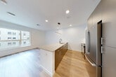 This thoughtfully designed 1-bedroom, 1-bathroom unit offers a clean, modern aesthetic highlighted by light hardwood flooring, crisp white walls, and recessed lighting throughout. The open-concept kitchen and living area serves as the heart of the unit, anchored by a sleek peninsula with a light stone countertop, an undermount sink with a matte black faucet, and dark cabinetry with brushed hardware. Stainless steel appliances—including a refrigerator, range, and microwave—complete the kitchen, which is further enhanced by a contemporary linear pendant light. A bright hallway connects the living space to the private areas of the unit, lined with multiple closets offering generous storage. The bedroom is a calm, well-lit retreat featuring a large window with views of the surrounding neighborhood. A versatile den provides additional flexible living space. The bathroom features a glass-enclosed shower, stone-tiled flooring, and warm wood-toned cabinetry, complemented by matte black fixtures that add a modern touch. The overall ambiance is bright, clean, and contemporary, making efficient use of its well-organized single-floor layout.