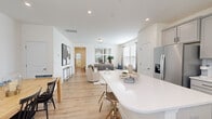 This well-designed two-story home offers a thoughtful layout spread across two floors, with the main level dedicated to communal living and the upper floor housing private quarters. The main level showcases an open-concept kitchen, dining, and living area bathed in natural light from multiple windows. The kitchen is outfitted with gray shaker cabinets, white quartz countertops, subway tile backsplash, stainless steel appliances, and a large island with bar seating. Light wood-look flooring flows throughout the main level, enhancing the bright, airy atmosphere. A half bathroom on this floor adds convenience for guests.

The living room provides a comfortable gathering space, while the adjacent dining area accommodates a full-sized table beneath a decorative round mirror. A staircase connects to the upper floor, where two bedrooms, an office, and two full bathrooms are located. The spacious primary bedroom features multiple windows, plush carpet, and a walk-in closet. The secondary bathroom includes gray vanity cabinetry and tile flooring. The dedicated office offers carpeted flooring and a window with natural light. Throughout, the home maintains a clean, neutral palette with consistent modern finishes.