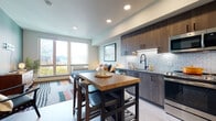 This thoughtfully designed studio unit offers a seamless open-concept layout that integrates the living, sleeping, and kitchen areas into a cohesive, functional living space. Light wood-style flooring flows throughout, complementing the clean, contemporary aesthetic.

The kitchen is a standout feature, showcasing rich dark wood cabinetry with matte black hardware, a herringbone tile backsplash, stone countertops, and a full suite of stainless steel appliances including a French door refrigerator, dishwasher, and range. A butcher block island provides additional prep space and casual seating for multiple guests.

The sleeping area is generously proportioned and anchored by a bold deep green accent wall, creating a cozy, stylish retreat. A walk-in closet with built-in shelving provides ample storage.

Large windows flood the space with natural light and frame striking views of the city skyline and surrounding mountains, giving the unit an open, airy feel. A sliding door off the entry hall adds a sleek, space-saving design element.

The bathroom features a dark wood vanity with an undermount sink, stone countertop, and a large mirror, paired with clean tile flooring. The overall ambiance is modern and sophisticated, blending comfort with urban elegance.