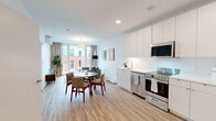 Located at 9 E Pleasant St in downtown Amherst, MA, this one-bedroom, one-bathroom unit offers a thoughtfully designed, modern living space. The open-plan main area seamlessly integrates the kitchen, dining, and living zones, creating an efficient yet comfortable layout. Light wood-style flooring runs throughout the main living area, contributing to a clean, contemporary aesthetic.

The kitchen is outfitted with a full suite of stainless steel appliances, including a range, over-the-range microwave, dishwasher, and refrigerator. Flat-front white cabinetry extends to the ceiling, maximizing storage, while white countertops maintain a crisp, minimalist look. Large windows in the living area allow natural light to fill the space and provide views of the surrounding streetscape.

The bedroom features a wall-mounted mini-split HVAC unit, a large window with outdoor views, and direct access to a dedicated walk-in closet with built-in wire shelving and hanging rods. The bathroom includes a shower/tub combination, white vanity, and wood-style flooring consistent with the rest of the unit. Throughout, the space maintains a bright, neutral palette that emphasizes a clean, modern character.
