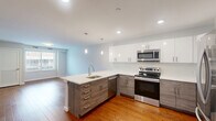 Located at 3857 Pechin Street in Philadelphia's Roxborough neighborhood, this well-appointed one-bedroom, one-bathroom unit offers a thoughtfully designed single-floor layout. The open-concept kitchen and living area serves as the heart of the space, showcasing warm hardwood flooring, recessed lighting, and elegant pendant lights above a peninsula island with a crisp white quartz countertop and undermount sink. The kitchen is outfitted with two-tone cabinetry — white upper cabinets paired with wood-grain lower cabinets — and a full suite of stainless steel appliances, including a French door refrigerator, electric range, microwave, and dishwasher. The living area flows naturally from the kitchen, bathed in natural light from a window overlooking the neighborhood streetscape. The bedroom features soft carpeting, neutral walls, and a generously sized window that brings in ample natural light. The full bathroom is finished with clean white subway tile surrounding a soaking tub and shower combination with chrome fixtures. A dedicated laundry room provides added convenience with a stacked washer and dryer unit. A closet rounds out the functional layout, making this a complete and efficient living space.