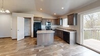 This two-story residence is efficiently organized across two levels, with the compact entry level serving as a transitional space that leads to the main living areas above via a straight staircase. The staircase features wood-grain vinyl treads with white risers and a rich, dark wood handrail, providing a clean and polished transition between floors.

The main level hosts the majority of the living space, where the kitchen stands out as a central feature. It is equipped with dark walnut-toned cabinetry, granite-style countertops, black appliances including a refrigerator, range, microwave, and dishwasher, and a central island that adds prep and storage functionality. Vaulted ceilings and recessed lighting elevate the space, while a sliding glass door provides natural light and outdoor access. An adjacent walk-in pantry/closet offers dedicated storage.

The bedroom is a well-proportioned room finished with plush carpet, a ceiling fan with light fixture, and a window that allows natural light and neighborhood views. An additional carpeted room with an electrical panel is also present on the main level. Wood-look flooring runs throughout the main living and kitchen areas, contributing to a cohesive and contemporary aesthetic throughout the home.
