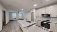 Located at 17448 N Eldridge Parkway in Tomball, Texas, this well-appointed one-bedroom, one-bathroom residence offers a thoughtfully designed single-floor layout with modern finishes throughout. The open-concept kitchen and living area serves as the heart of the home, anchored by a central island featuring striking granite countertops and an undermount sink. The kitchen is fully equipped with stainless steel appliances, including a French door refrigerator, range, and built-in microwave, complemented by light wood-tone cabinetry and a tile backsplash. Wood-look plank flooring extends through the main living areas, providing a clean, cohesive aesthetic, while recessed lighting and a ceiling fan keep the space bright and comfortable. The living room receives natural light through large windows fitted with blinds. The bedroom offers plush carpeting, a ceiling fan, and a well-sized window that fills the room with natural light. The bathroom features a tiled tub and shower combination, granite vanity, and direct access to a walk-in closet with built-in shelving. An in-unit laundry area with a washer connection adds everyday convenience. The overall design palette of neutral grays and warm whites creates a clean, modern ambiance throughout.