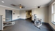 Located at 30 Maryland Ave in Rockville, Maryland, this fitness center is a well-appointed, single-floor facility designed to support a comprehensive workout experience. The space is divided into distinct exercise zones, each outfitted with dedicated equipment to accommodate a variety of fitness routines.

The main workout area features durable rubber flooring throughout, providing both safety and comfort underfoot. Cardio equipment includes treadmills and an elliptical machine, several of which are equipped with individual monitors for entertainment during exercise. Strength training is supported by multiple cable and resistance machines, as well as a multi-function weight station. A full-length mirrored wall in one section visually expands the space and allows users to monitor their form.

Crown molding and neutral-toned walls lend a polished, upscale aesthetic to the interior. Recessed lighting and ceiling fans ensure the space remains well-lit and comfortable. A water fountain is conveniently located within the facility, and built-in shelving near the entrance provides storage for personal items.

Natural light flows in through large windows and glass-paned doors that open directly to an outdoor patio area, offering views of the surrounding courtyard. This seamless indoor-outdoor connection enhances the overall ambiance, making the fitness center a bright and inviting environment for daily use.