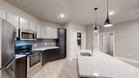 This thoughtfully designed 2-bedroom, 2-bathroom residence in Little Rock, Arkansas offers a clean, contemporary aesthetic throughout. The open-concept kitchen and living area serves as the heart of the home, anchored by a central island with a granite countertop and integrated sink, illuminated by sleek pendant lighting. The kitchen is well-equipped with stainless steel appliances, including a refrigerator, range, and microwave, complemented by two-tone cabinetry — white upper cabinets and dark espresso lower cabinets — set against a gray subway tile backsplash. Light wood-look flooring runs throughout the main living areas, adding warmth and continuity. Both bedrooms feature plush carpeting and ceiling fans, with the primary bedroom offering en-suite access to a bathroom complete with a granite-topped vanity and a walk-in glass shower. The second bedroom enjoys natural light from a window with outdoor views. The second bathroom is equipped with a full tub-shower combination and additional cabinet storage. Two closets provide ample storage throughout the unit. The overall palette of soft grays, whites, and warm neutrals creates a cohesive and inviting atmosphere throughout this well-planned single-level residence.