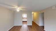This single-floor residence offers a well-organized layout designed for comfortable everyday living. The spacious living room serves as the heart of the home, featuring warm wood-look flooring, neutral-toned walls, and a ceiling fan with integrated lighting. A sliding glass door fitted with vertical blinds opens to an outdoor green view, allowing natural light to fill the space. The living area flows conveniently toward the kitchen, which is accessed through an open archway. The kitchen is equipped with white cabinetry, dark granite-style countertops, a double stainless steel sink beneath a window, a black electric range with an overhead exhaust hood, and a classic subway tile backsplash. A hallway with wood-look flooring connects the main living spaces to the private areas of the home. The bedrooms are carpeted and finished with soft neutral tones, each featuring windows with blinds that admit ample natural light. The bathroom is clean and functional, offering a full-size soaking tub and shower combination with chrome fixtures, a vanity with a sink, and a mirror. Throughout the unit, consistent neutral paint tones and white trim create a cohesive, move-in-ready aesthetic.