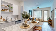 Located at 7311 Baymeadows Way in Jacksonville, FL, this thoughtfully designed one-bedroom, one-bathroom residence offers a modern and efficient layout across a single floor. The open-concept living area seamlessly integrates the kitchen, dining, and living spaces, creating an inviting and functional environment. The kitchen is a standout feature, boasting granite countertop surfaces, white cabinetry, stainless steel appliances, and a generous island with bar seating — ideal for both casual dining and entertaining. Light wood-style flooring flows throughout, complementing the bright, neutral color palette and recessed lighting. The living room is filled with natural light from large windows and a glass door that opens to a private balcony overlooking a landscaped exterior. The spacious bedroom offers a tranquil retreat with a sizable window, ample natural light, and access to two closets. The well-appointed bathroom features a double-sink granite vanity and a walk-in shower. A dedicated in-unit laundry room with a full-size washer and dryer adds everyday convenience. With a ceiling fan, clean architectural lines, and thoughtful finishes throughout, this residence delivers a comfortable and contemporary living experience.