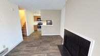 This two-story home offers a well-organized layout designed for comfortable everyday living. The main level centers around an open-concept living area finished with dark hardwood-style flooring that runs throughout, creating a cohesive and grounded aesthetic. A black-tiled fireplace anchors one wall of the living space, serving as a functional and visual focal point.

The kitchen is positioned adjacent to the living area and is accessible via a peninsula-style breakfast bar, which provides a natural division between the two spaces while maintaining an open feel. The kitchen is equipped with a gas range, black refrigerator, and black microwave, all complemented by warm-toned wood cabinetry. The breakfast bar adds convenient counter seating and enhances the space's usability.

A staircase located near the entry leads to the second floor, where additional living spaces are situated. The textured ceilings are consistent throughout the main level, and neutral wall tones in warm grey and beige contribute to a clean, move-in-ready atmosphere. Overall, the space balances practicality with a straightforward, functional design suited for a variety of lifestyles.