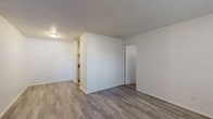 This single-floor, one-bedroom, one-bathroom unit at 11530 Holiday Dr in Kansas City, MO offers a practical and efficient layout across a compact but well-organized floor plan. The living areas feature wood-style plank flooring throughout, complemented by white walls and a textured ceiling that adds a classic touch. Natural light enters through windows fitted with blinds, brightening both the living room and bedroom spaces. A wall-mounted HVAC unit provides climate control in the main living area. The living room flows openly into a secondary living or dining area, with clean sightlines and a neutral color palette throughout. The kitchen is laid out in a galley style, featuring white cabinetry, warm-toned countertops, a double-basin sink, and appliances including a range and refrigerator. The bedroom is a comfortable, carpeted space with a window that lets in natural light, leading directly to a dedicated walk-in closet equipped with wire shelving on both sides for organized storage. The bathroom includes a full tub-shower combination, a toilet, and a single vanity with a mirror. The unit's clean, understated design provides a functional and move-in-ready living environment.