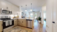 This thoughtfully designed 1-bedroom, 1-bathroom residence offers a cohesive open-concept layout that seamlessly connects the kitchen and living area. The kitchen is a standout feature, appointed with granite countertops, a large peninsula with bar seating, two-tone cabinetry combining white upper cabinets with warm wood lower cabinets, a full suite of stainless steel appliances, and stylish pendant lighting overhead. Light wood-tone flooring runs throughout the entire space, contributing to a bright and airy atmosphere. The living room receives generous natural light through multiple windows and a glass-panel door that opens to an outdoor area, and is equipped with a ceiling fan for added comfort. The bedroom is a serene retreat, featuring large windows that allow abundant natural light, a ceiling fan, and direct access to a spacious walk-in closet outfitted with multiple hanging rods and shelving. The bathroom includes a granite-topped vanity with under-mount sink, white cabinetry with matte black hardware, and a full tub-shower combination. Crisp white walls and a neutral palette are consistent throughout, creating a clean and modern aesthetic that is both functional and inviting.