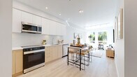 This thoughtfully designed two-bedroom, one-bathroom unit in Richmond, British Columbia offers a clean, contemporary aesthetic throughout its efficiently laid-out single floor. Light wood laminate flooring flows seamlessly across the living spaces, complementing the bright, neutral palette that defines the interior. The living room is a welcoming, sun-drenched space featuring large windows that frame views of lush greenery and the surrounding neighbourhood, with track lighting overhead adding a modern touch. The kitchen is well-equipped with stainless steel appliances, a combination of white upper cabinets and warm wood lower cabinetry, a subway tile backsplash, and a marble-topped island that doubles as a dining area. The primary bedroom benefits from generous window placement, filling the room with natural light and offering pleasant outdoor views, while a built-in closet provides practical storage. The second bedroom is equally bright and comfortable. The bathroom presents a polished finish with large-format marble-look floor tiles, a floating wood vanity with a white countertop, and a full soaker tub with shower. A hallway connects all rooms efficiently, contributing to the unit's smart and functional flow.