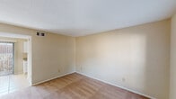 This single-story unit in Conroe, Texas, features a practical and well-organized floor plan with two bedrooms and one bathroom. The layout, visible in the overhead scan, connects a kitchen, living area, bedrooms, and bathroom in a compact, efficient arrangement.

The bedrooms are carpeted in neutral tan tones and finished with warm beige walls, white baseboards, and textured ceilings. Each room includes windows fitted with horizontal blinds, allowing natural light to filter in while providing outdoor views of the surrounding greenery and exterior structures. Ceiling-mounted HVAC vents are present throughout, supporting year-round climate control.

The kitchen features white cabinetry with ample upper and lower storage, speckled countertops, a double stainless steel sink, and white appliances including an electric range and refrigerator. Light tile flooring grounds the space and contrasts with the carpeted areas throughout the rest of the unit.

The bathroom area includes a vanity with white cabinetry, a granite-style countertop, a single sink, and a lighted mirror above. The overall palette across all rooms is consistent — warm neutrals with white trim — giving the unit a cohesive, clean appearance throughout.