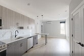 Unit 404 at 1213–1221 Broad St is a thoughtfully designed two-bedroom, one-bathroom residence that combines modern aesthetics with functional living. Light hardwood flooring flows consistently throughout the space, complementing the neutral gray and white color palette found in every room.

The kitchen is a standout feature, showcasing floor-to-ceiling cabinetry in a warm taupe wood-grain finish paired with crisp white quartz countertops and a white subway tile backsplash. A full suite of stainless steel appliances — including a GE range, microwave, refrigerator, and dishwasher — and a matte black faucet complete the modern look.

The primary bedroom offers a comfortable footprint with a large window that invites natural light and provides pleasant outdoor views of the surrounding neighborhood. A double-door closet adds practical storage. The second bedroom features the same clean design language with light walls, hardwood floors, and a double closet, making it versatile for various uses.

The bathroom is finished with matte black hardware and grab bar details, reflecting thoughtful, accessible design. White panel-style doors with matte black hardware carry a consistent modern style throughout. The overall ambiance is clean, bright, and contemporary, ideal for those seeking a move-in-ready residence with quality finishes.