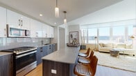 Located at 45 Main St in Yonkers, NY, this thoughtfully designed single-floor residence offers a seamless blend of contemporary style and functional living. The open-concept kitchen and living area serve as the heart of the home, anchored by a central island with bar seating and pendant lighting overhead. The kitchen is outfitted with stainless steel appliances, including a gas range, microwave, and refrigerator, complemented by two-tone cabinetry — gloss white uppers and dark wood lowers — set against a sleek gray backsplash. Light wood flooring flows throughout, enhancing the bright, airy atmosphere. The living room benefits from floor-to-ceiling windows that frame expansive waterfront views and flood the space with natural light. A dedicated den provides a versatile flex space, also enjoying scenic views through a large window. The primary bedroom is generously proportioned with wide windows overlooking the water, while the primary bathroom features a double vanity with wood cabinetry, large-format tile flooring, and a glass-enclosed walk-in shower. A second bedroom and a second full bathroom with a soaking tub and tiled surround round out the layout. An in-unit stacked washer and dryer adds everyday convenience to this well-appointed residence.