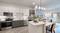 This thoughtfully designed one-bedroom, one-bathroom residence offers a well-appointed single-floor layout that maximizes functionality and style. The open-concept kitchen and living area serves as the heart of the home, anchored by a central island with a crisp white countertop and a modern multi-arm pendant chandelier above. The kitchen is outfitted with two-tone cabinetry — white upper cabinets paired with charcoal lower cabinets — set against a classic white subway tile backsplash. A full suite of stainless steel appliances, including a refrigerator, dishwasher, range, and microwave, completes the space. Light wood-tone luxury vinyl plank flooring flows throughout, lending warmth and continuity. The living room benefits from soaring ceilings and a set of French doors that open to a private outdoor balcony, flooding the space with natural light. The spacious bedroom features elevated ceilings, a walk-in closet, and a window with outdoor views, creating a calm and restful retreat. The full bathroom includes a soaking tub with shower combination and wood-look tile flooring. A dedicated in-unit stacked washer and dryer adds everyday convenience, rounding out this efficiently designed and modern residence.