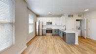 Located at 725–735 Coleman Blvd in Mount Pleasant, South Carolina, this one-bedroom, one-bathroom unit offers a thoughtfully designed layout that maximizes every square foot. Light wood-tone flooring flows consistently throughout the space, creating a warm, cohesive aesthetic.

The kitchen is a standout feature, outfitted with two-tone cabinetry — crisp white upper cabinets paired with sage gray lower cabinets — complemented by a white subway tile backsplash and light quartz countertops. Stainless steel appliances, including a refrigerator, range, microwave, and dishwasher, complete the space. A window allows natural light to brighten the kitchen area.

The open living area adjoins the kitchen and benefits from additional natural light through multiple windows dressed with white horizontal blinds. A ceiling fan overhead adds both function and comfort to the space.

The bedroom is well-proportioned, featuring multiple windows that invite natural light and provide views of the surrounding greenery. A ceiling fan and light wood flooring continue the unit's clean, consistent design language. A dedicated closet provides practical storage.

The bathroom is finished with light neutral tones and includes a full tub-and-shower combination with a curved curtain rod, bronze fixtures, and wood-look flooring that ties the space together cohesively.