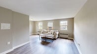 Located at 1408–1410 W Abingdon Dr in Alexandria, VA, this two-bedroom, one-bathroom residence offers a practical and well-organized single-floor layout. The living room is a welcoming, open area finished with light hardwood-style flooring and neutral taupe walls. Multiple windows line the room, allowing abundant natural light to fill the space while offering views of the surrounding greenery. Baseboard radiators and wall-mounted AC units provide year-round climate control throughout.

The kitchen is efficiently laid out with white cabinetry, a gas range, stainless steel refrigerator, and over-the-range microwave, offering essential functionality in a compact footprint. Light wood-tone flooring carries through from the main living areas.

The primary bedroom features two closets with hanging rods, neutral walls, a window with outdoor views, and the same hardwood-style flooring found throughout the unit. The second bedroom is similarly appointed, with a window and its own closet for ample storage.

The bathroom includes a full tub and shower combination with white tile surround and a window that brings in natural light and outdoor views. A connecting hallway ties all rooms together seamlessly, contributing to the efficient and cohesive flow of the overall floor plan.