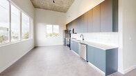 Located at 315 NW 32nd St in Miami's vibrant Wynwood neighborhood, this thoughtfully designed one-bedroom, one-bathroom unit delivers a clean, contemporary aesthetic throughout its single floor. Soaring ceilings amplify the sense of openness, while large-format light grey porcelain tile flooring flows seamlessly from room to room, grounding the bright, minimalist interiors.

The galley-style kitchen is a standout feature, showcasing floor-to-ceiling slate-blue cabinetry, white subway tile backsplash, crisp white countertops, and a full suite of stainless steel appliances including a French-door refrigerator, electric range, over-the-range microwave, and dishwasher. An exposed concrete ceiling detail adds an industrial edge that nods to the surrounding Wynwood arts district.

The spacious bedroom is bathed in natural light through oversized windows that frame lush greenery and Miami skyline views. Stylish capsule-shaped wall sconces provide warm accent lighting, and built-in shelving and double clothing rods offer well-organized storage. The bathroom features large-format wall and floor tile, a frameless glass walk-in shower with matte black fixtures, a dark-toned vanity with a white countertop, and a small window for natural ventilation. The overall ambiance is modern, airy, and move-in ready.